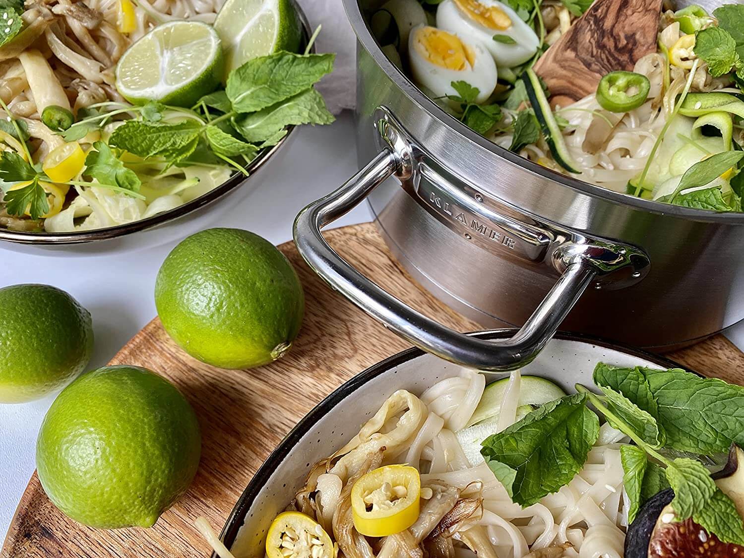 Edelstahl Topfset 4-teilig mit frisch zubereiteten Nudelgerichten, Limetten und frischen Kräutern.