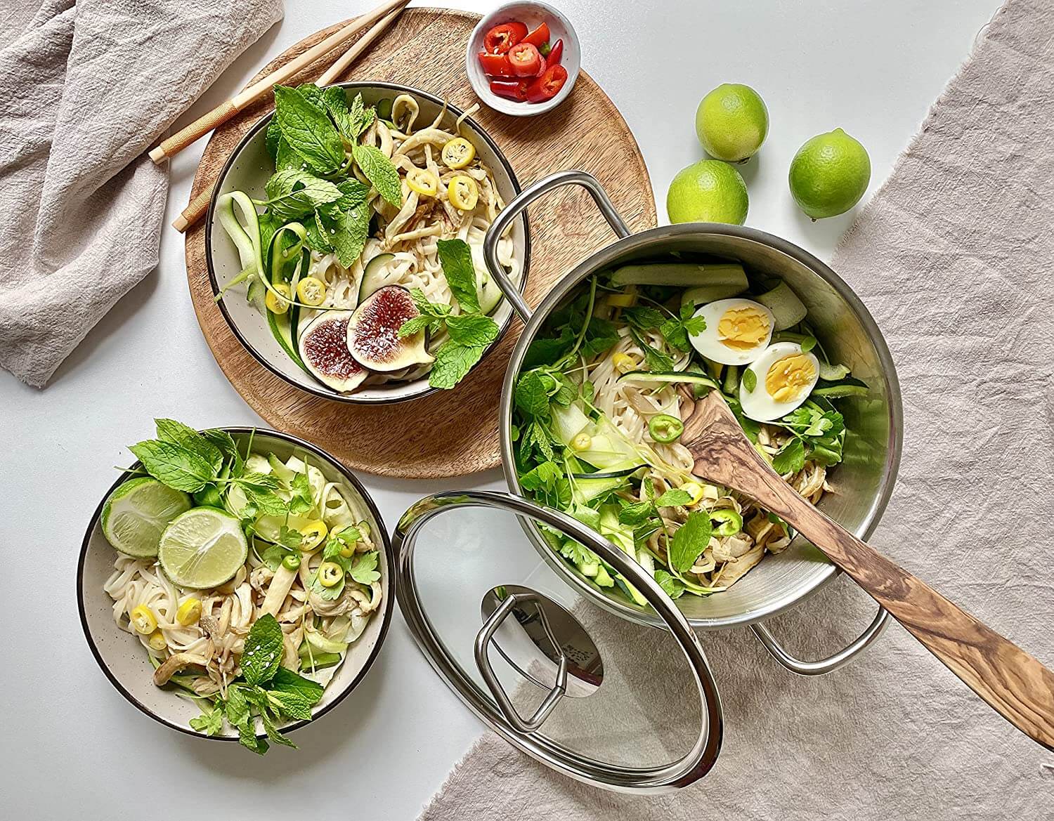 Edelstahl Topfset 4-teilig mit frischem Nudelgericht, Gemüse und Limetten auf einem Tisch.